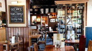 A restaurant interior with wooden furniture, a menu board, and a wine rack. - The Fox Inn by Greene King Inns (Bury St Edmunds)
