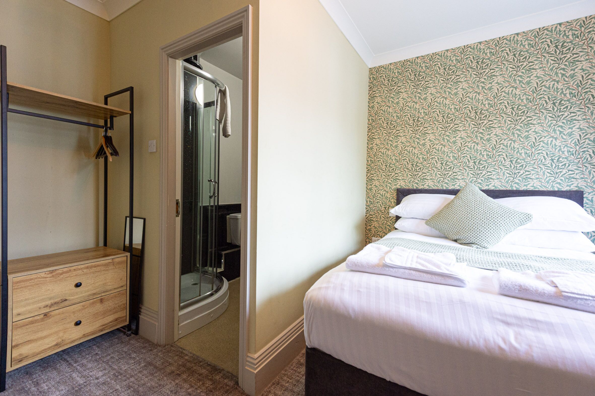 A bedroom with a bed, a wooden dresser, a mirror, and a shower area.