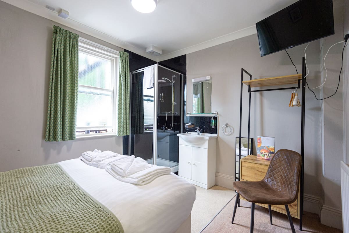A hotel room with a bed, a desk, a chair, a shower, and a TV.