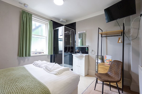 A hotel room with a bed, a desk, a chair, a shower, and a TV.