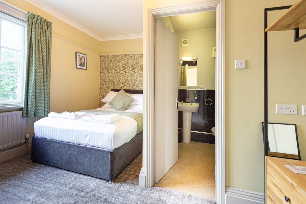 A hotel room with a bed, a bathroom with a sink and mirror, and a window with curtains.