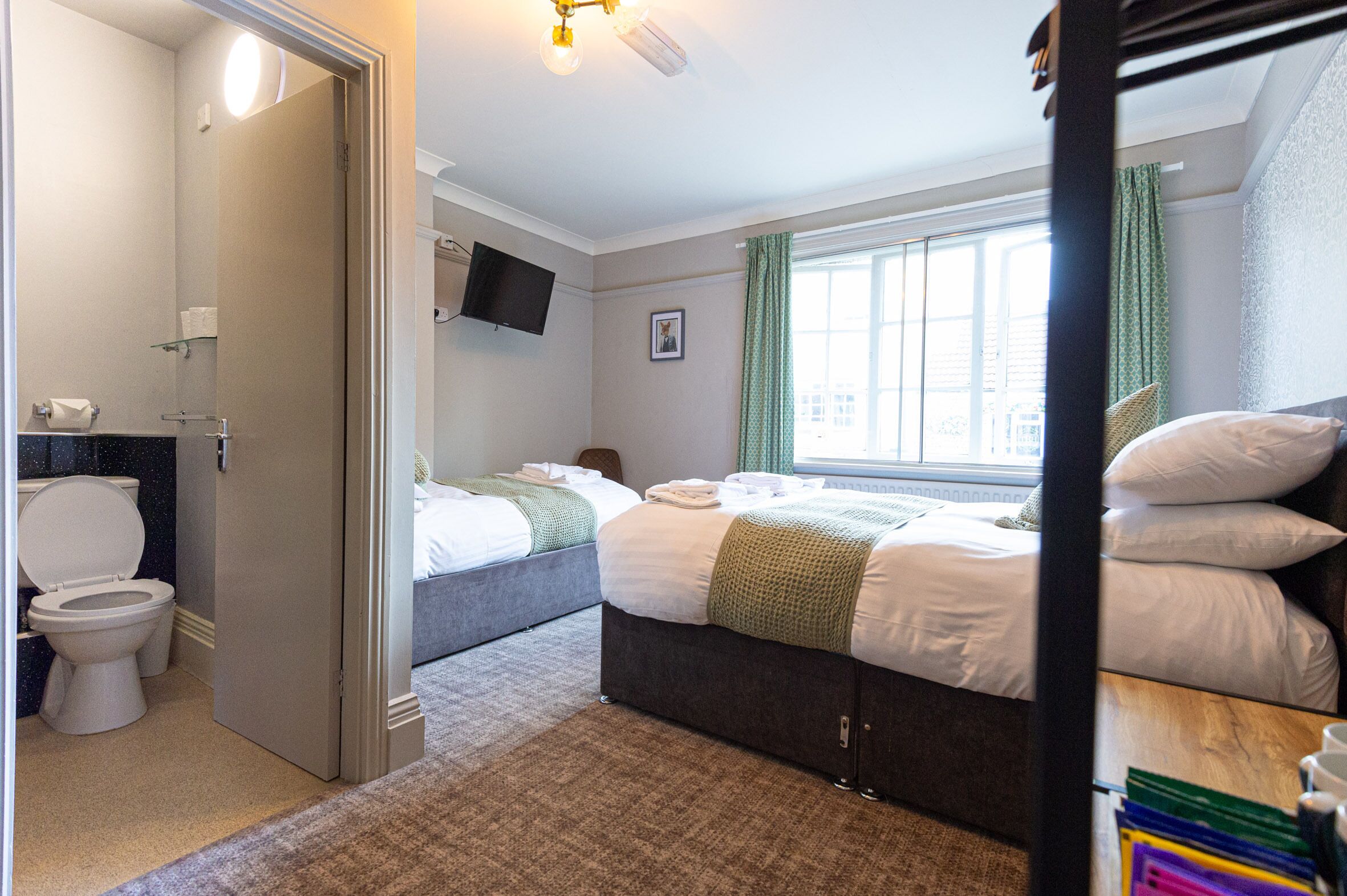 Une chambre d’hôtel avec deux lits, une salle de bain et un téléviseur fixé au mur.