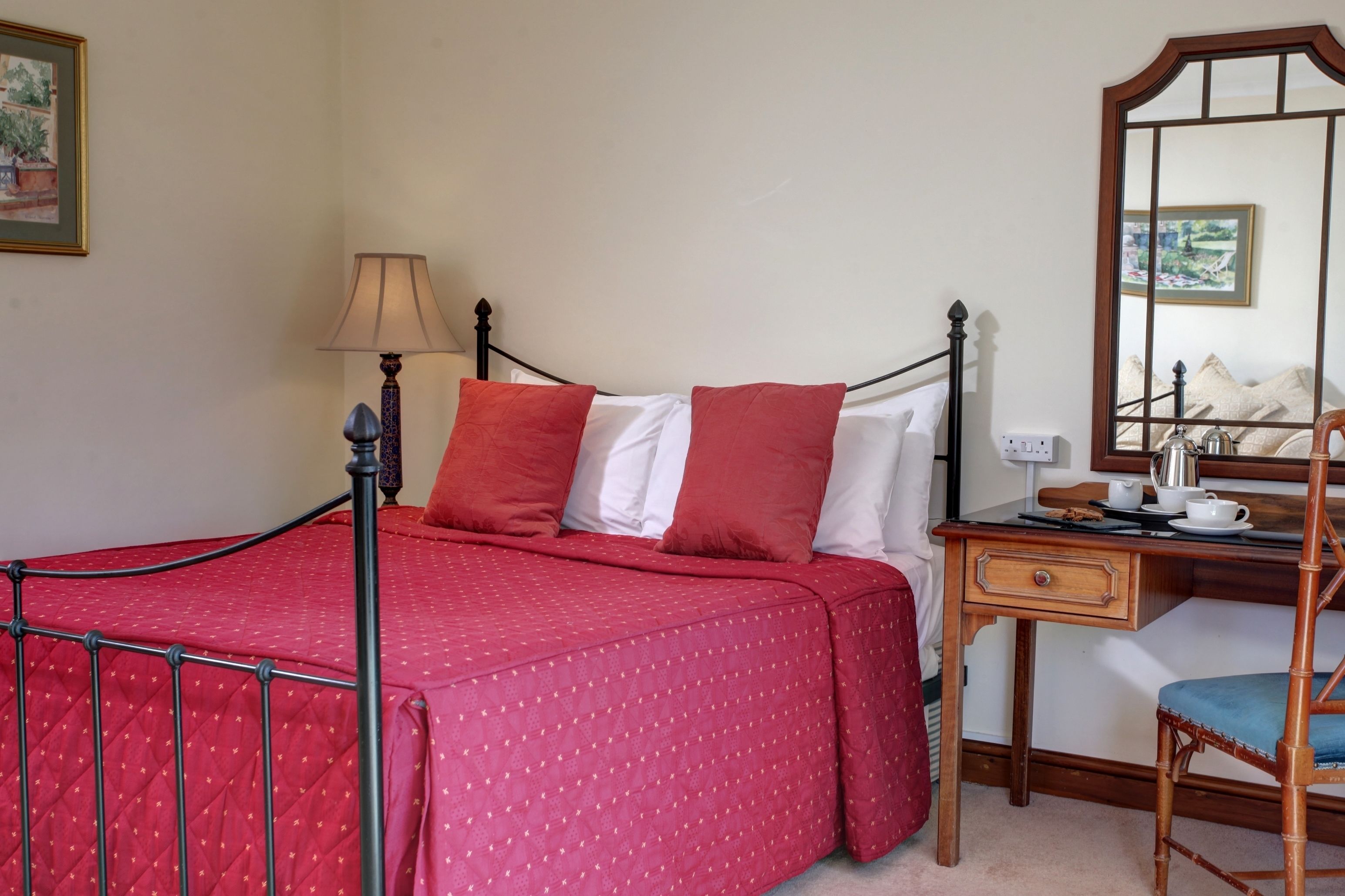 A neatly arranged bedroom with a bed, a bedside table with a lamp, a chair, and a mirror.
