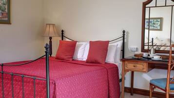 A neatly arranged bedroom with a bed, a bedside table with a lamp, a chair, and a mirror.