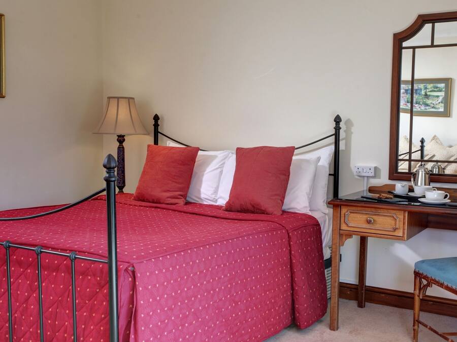 A neatly arranged bedroom with a bed, a bedside table with a lamp, a chair, and a mirror.