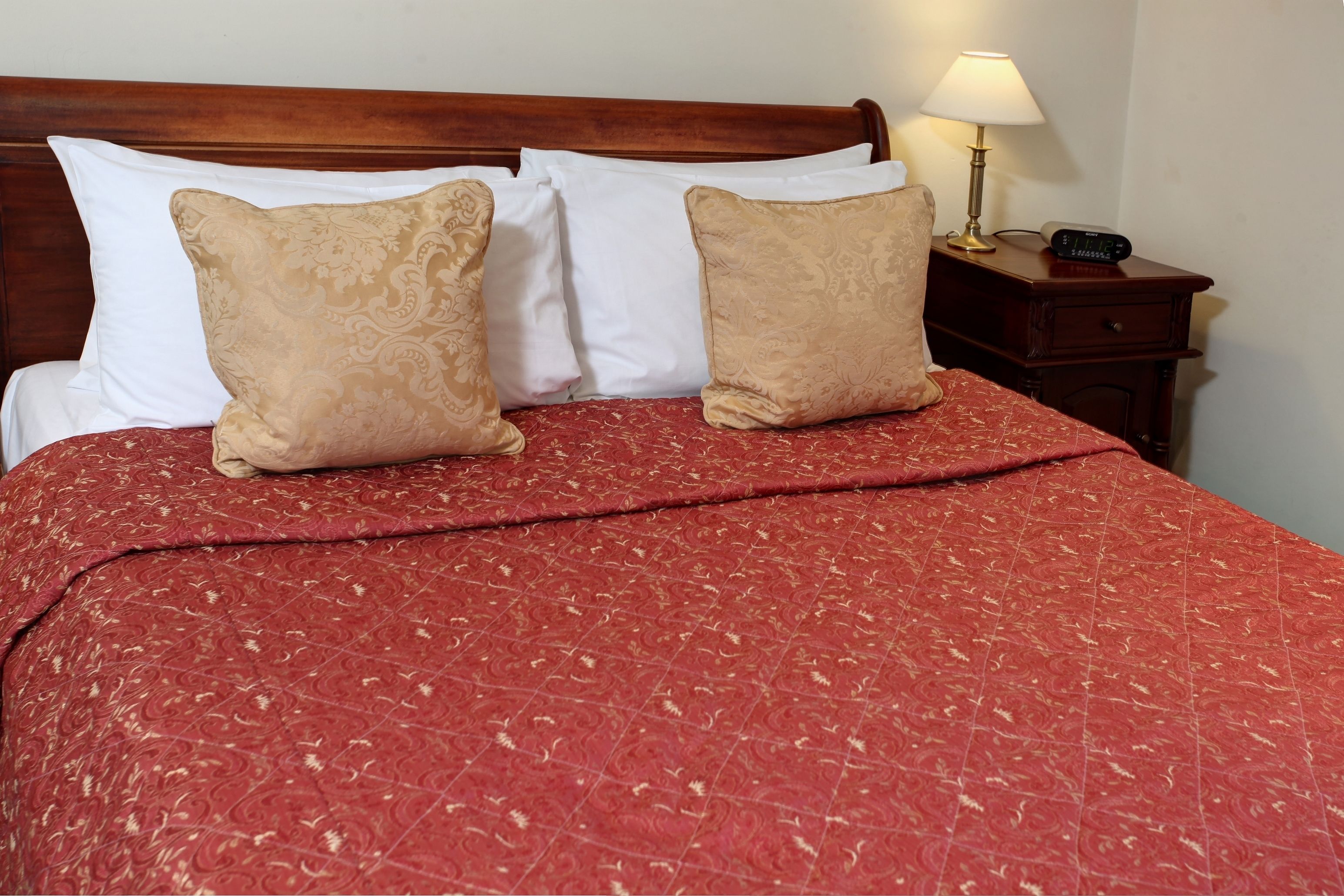 Een net opgemaakt bed met een rood gebedrukte sprei en twee beige kussens.