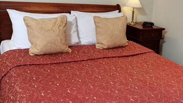 Een net opgemaakt bed met een rood gebedrukte sprei en twee beige kussens.