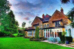 A traditional brick house with a large front lawn, a conservatory, and a patio with outdoor seating. - The Grange at Oborne (Sherborne)