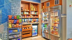 A well-organized snack and beverage section with various packaged foods and drinks, a small refrigerator, and a larger refrigerated display. - SpringHill Suites By Marriott Columbia Fort Meade Area (Columbia)