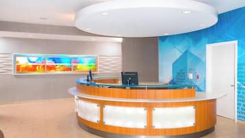 A modern reception desk with a digital screen, a flat-screen TV, and a wall with geometric patterns and text.