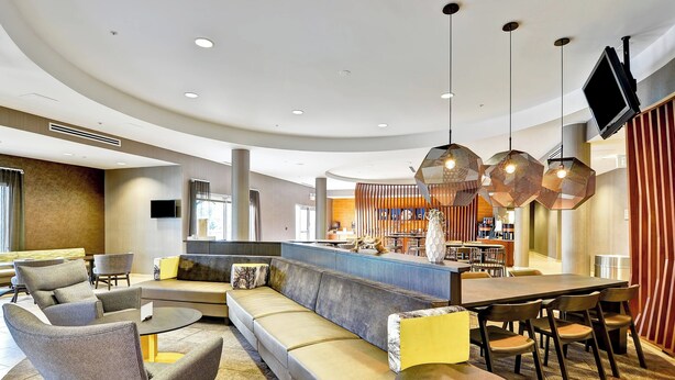 A modern lounge area with a curved seating arrangement, a bar, and a television mounted on the wall. - SpringHill Suites By Marriott Columbia Fort Meade Area (Columbia)