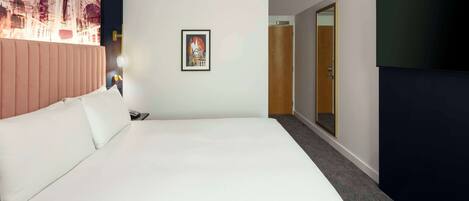 Habitación de hotel con una cama grande, un cuadro en la pared, un televisor a la derecha y una puerta que da a otra habitación.