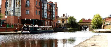A canal with a boat docked at a brick building with large windows and a staircase leading to an upper level.