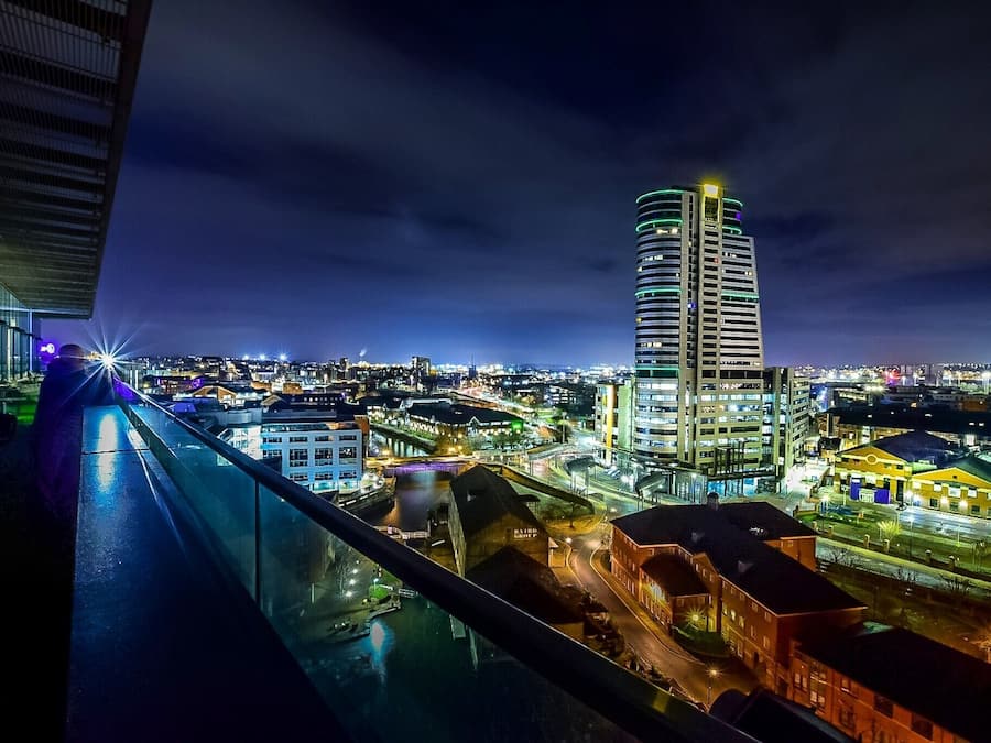 Paisatge urbà nocturn amb un edifici alt destacat, un riu i un pont.