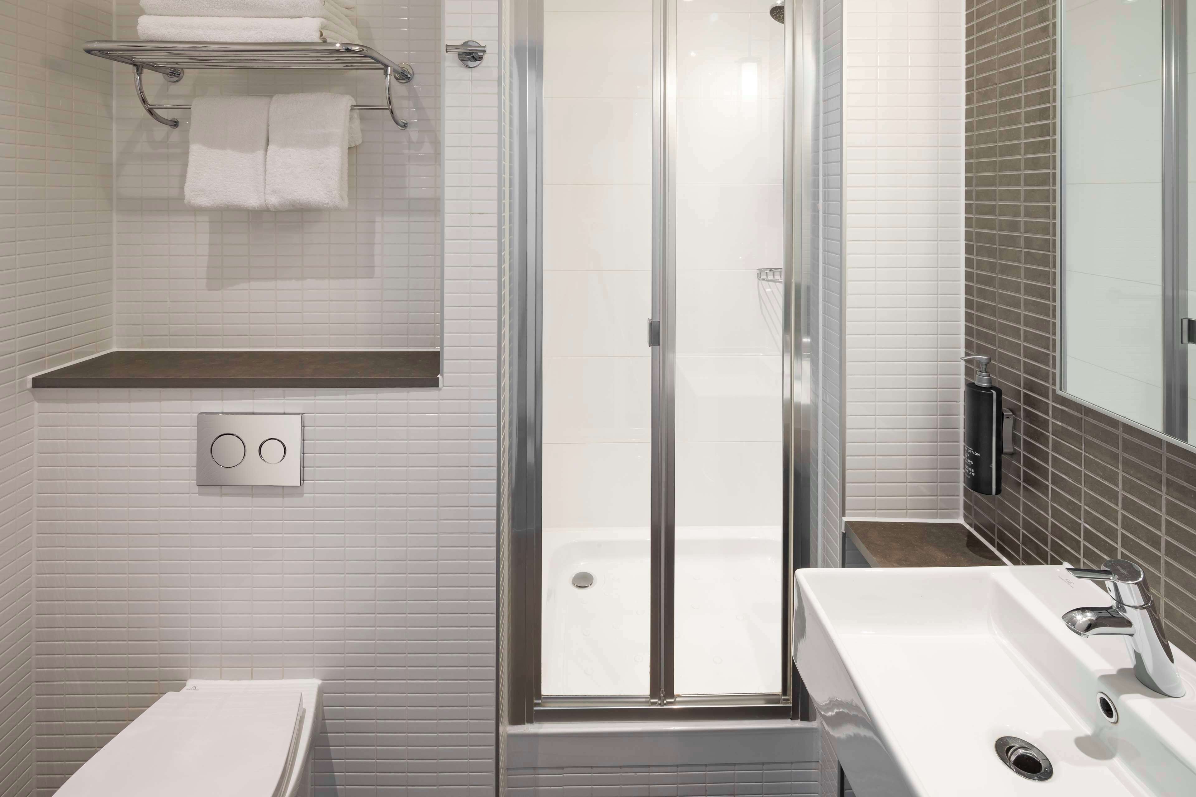 A modern bathroom with a glass-enclosed shower, a white sink, and a towel rack.