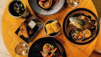 A round wooden table with various dishes including grilled fish, corn, and a salad.