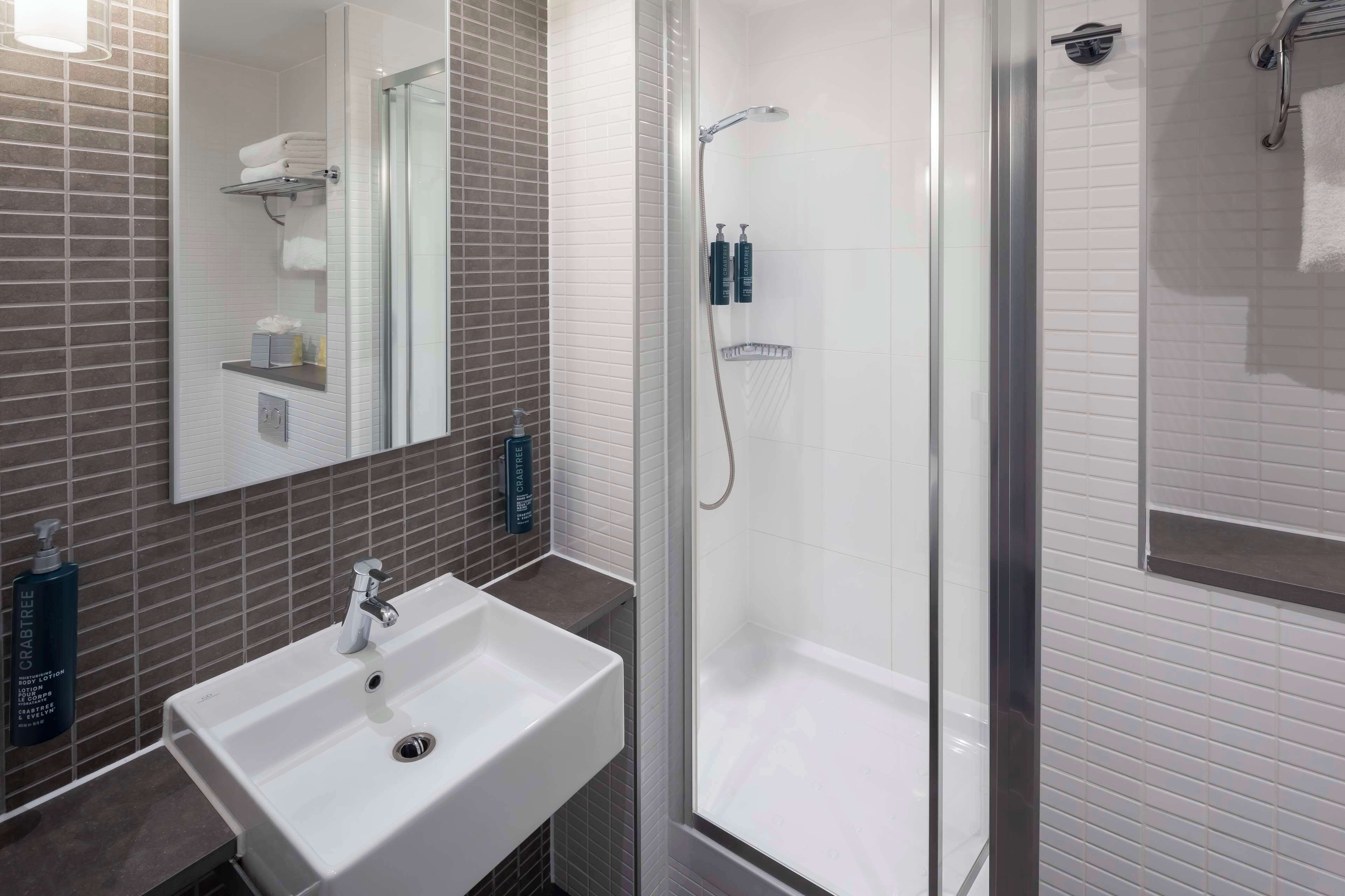 A modern bathroom with a white sink, a glass-enclosed shower, and a mirror above the sink.