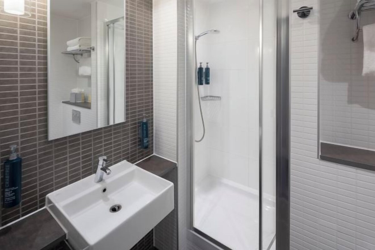 A modern bathroom with a white sink, a glass-enclosed shower, and a mirror above the sink.