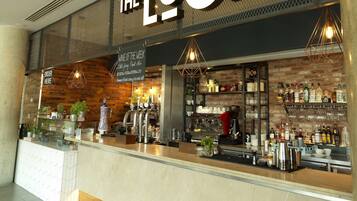 A bar named "The Lock" with a rustic brick wall, a wine selection display, and a variety of bottles and glasses on the counter.