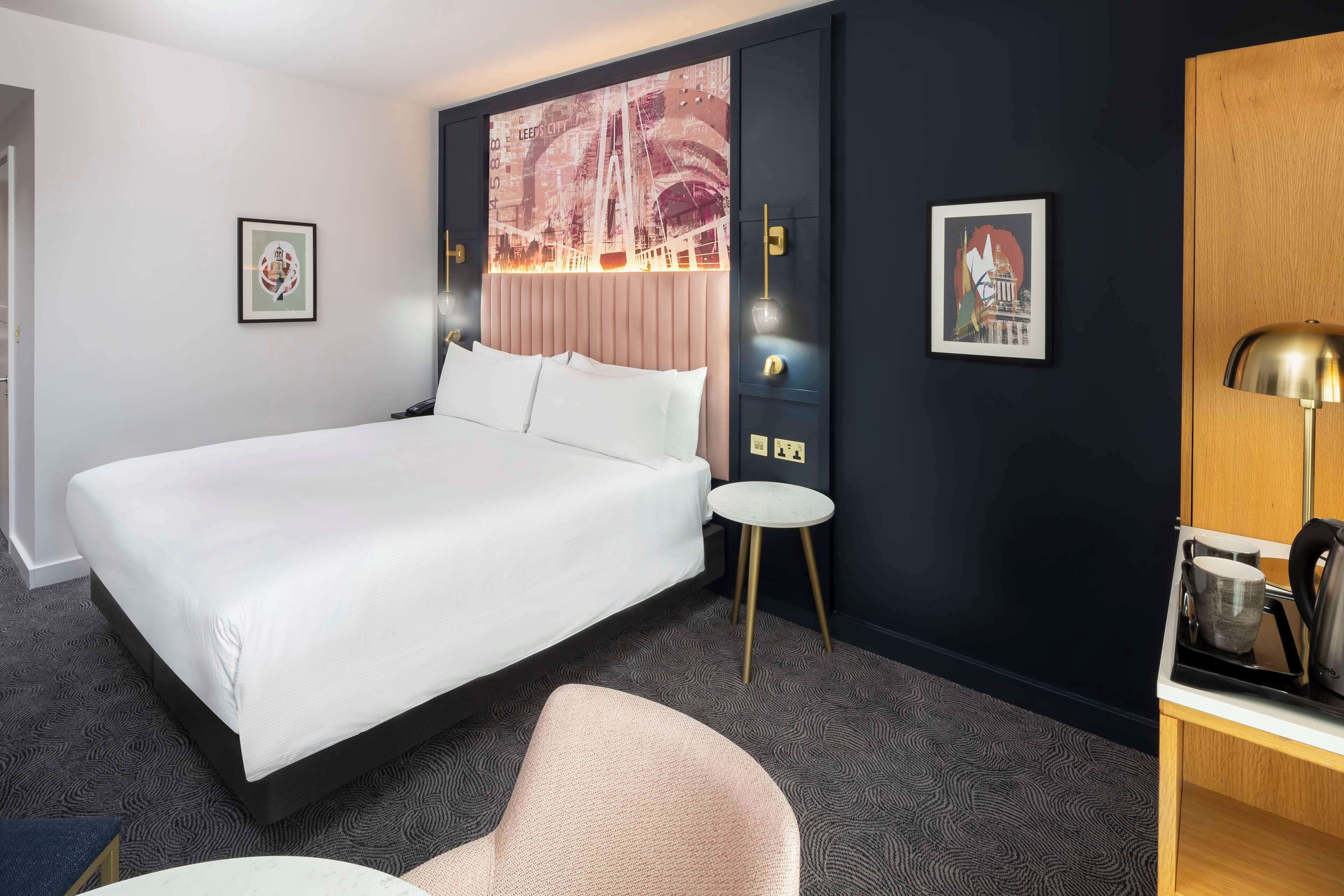 Una habitación de hotel con una cama grande, una mesita redonda pequeña, una silla y un escritorio con una lámpara.