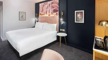 Una habitación de hotel con una cama grande, una mesita redonda pequeña, una silla y un escritorio con una lámpara.