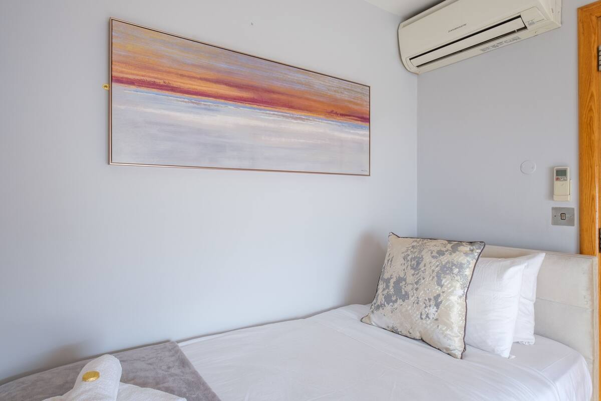 A bedroom with a bed, a pillow, a wall-mounted air conditioner, and a painting.
