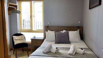 A bedroom with a bed, a chair, a desk, and a window with blinds.