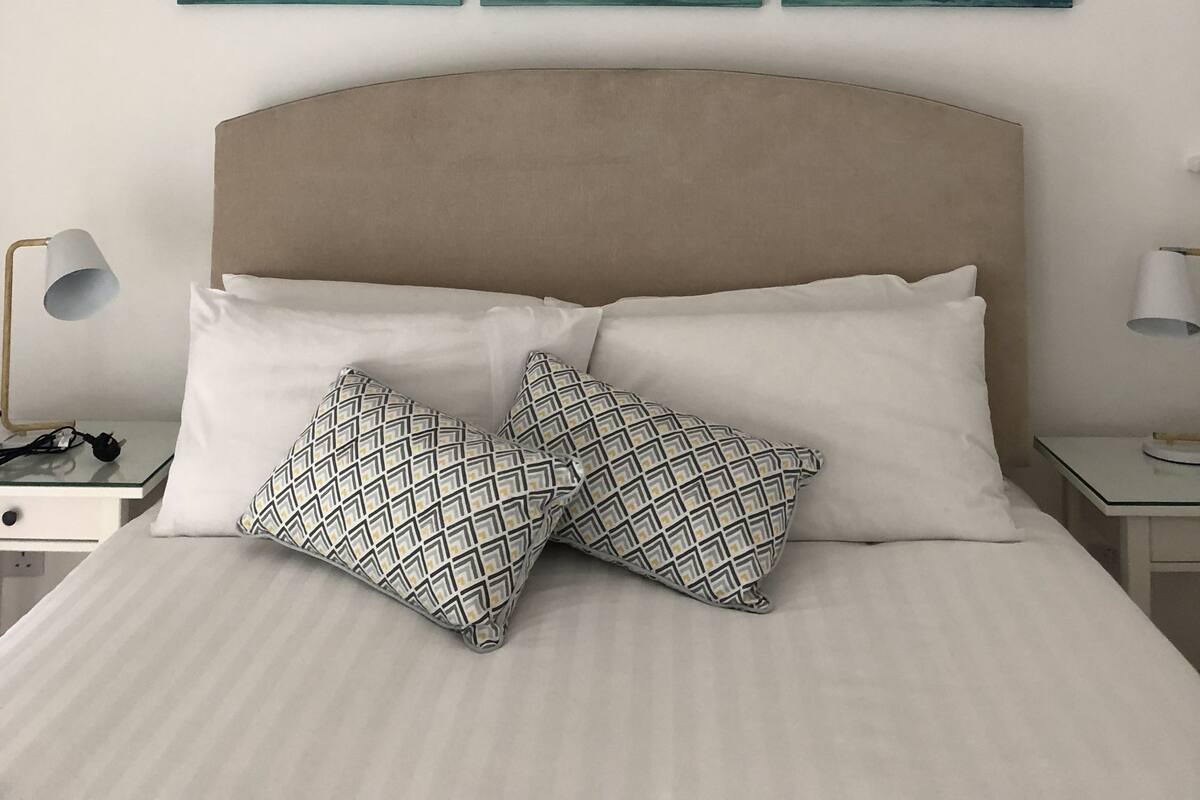 A bedroom with a bed, pillows, a nightstand, a lamp, and a wall-mounted artwork.