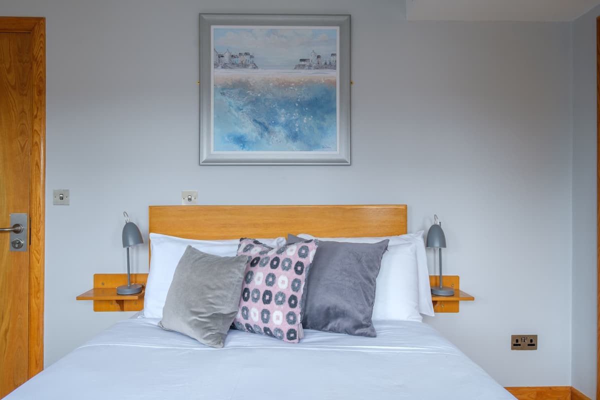 A neatly made bed with a wooden headboard, two bedside tables with lamps, and a framed painting above the bed.