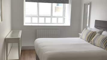 A bedroom with a large bed, a bedside table, a window with a view, a radiator, and a hanging light fixture.