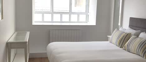 Un dormitorio con una cama grande, una mesita de noche, una ventana con vistas, un radiador y una lámpara colgante.