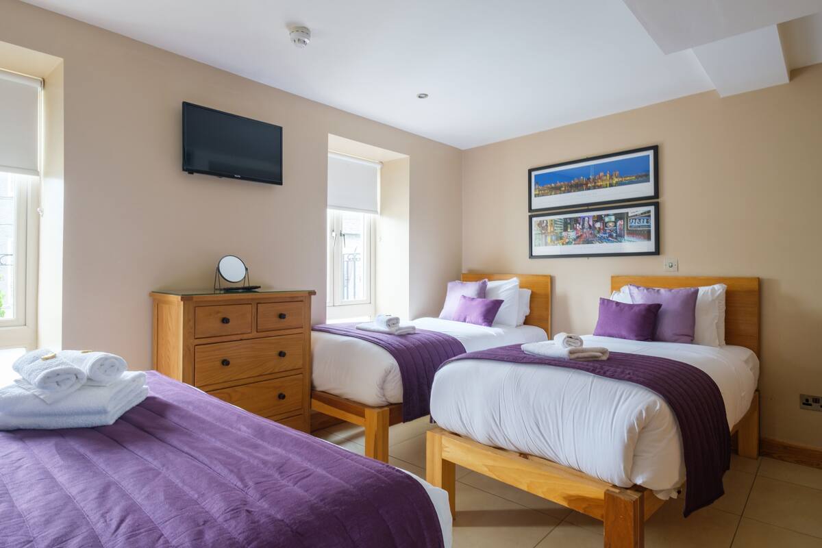 A hotel room with two beds, a wooden dresser, a flat-screen TV, and a window with blinds.