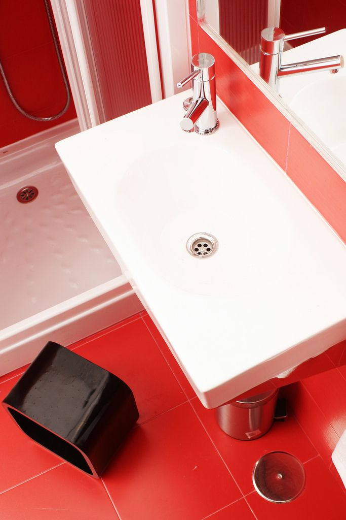 A bathroom with a white sink, chrome faucet, and red tiled floor.