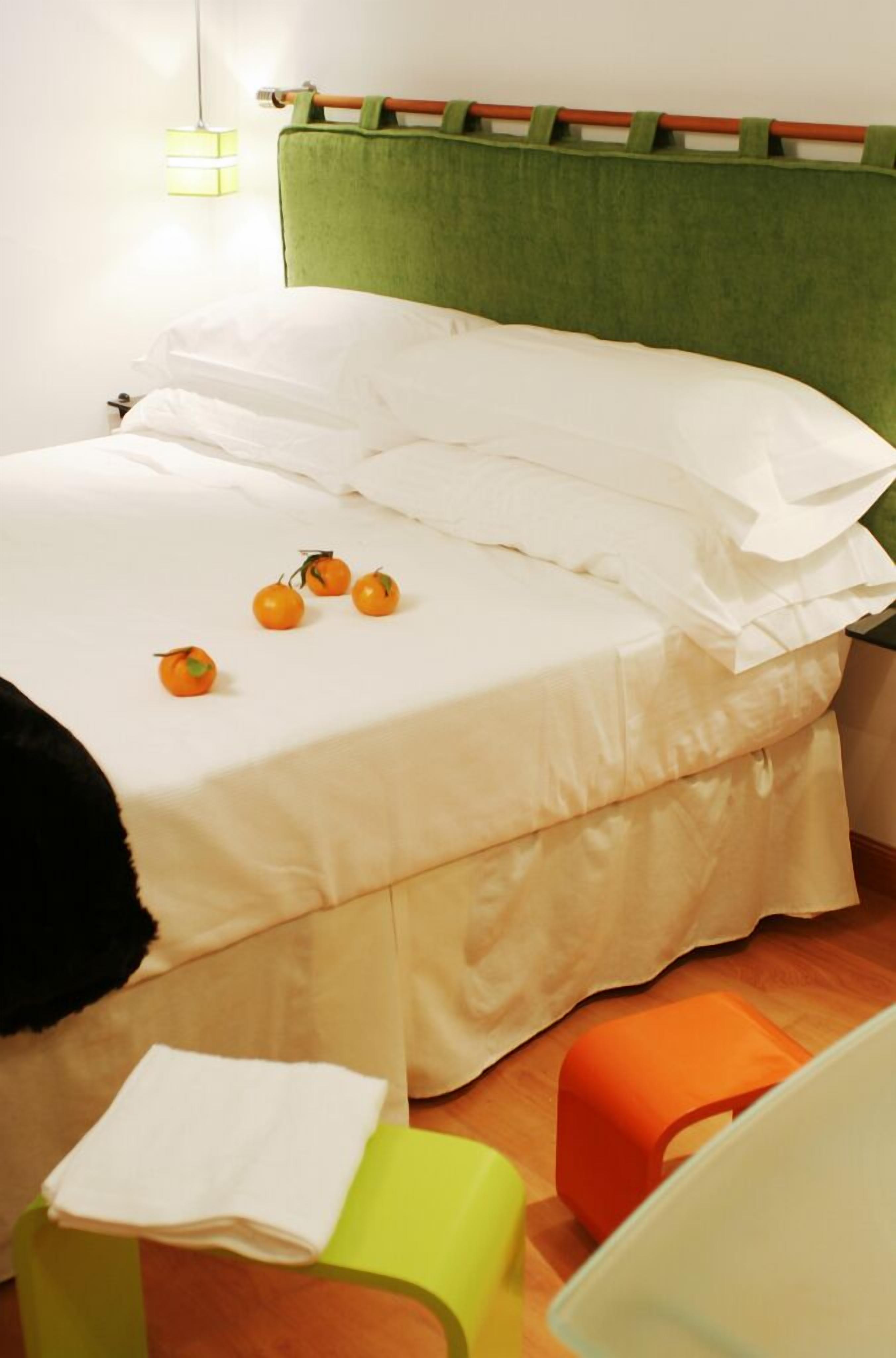 Una cama con ropa blanca, cabecera verde y una mesita con mantel blanco.