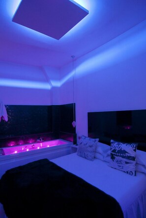 Un dormitorio moderno con tragaluces, una cama grande con almohadas, una mesita de noche y una ventana con vistas.
