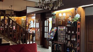 Un vestíbulo con un sofá rojo, una mesa de centro de madera, una araña, una recepción y una exhibición de recuerdos.