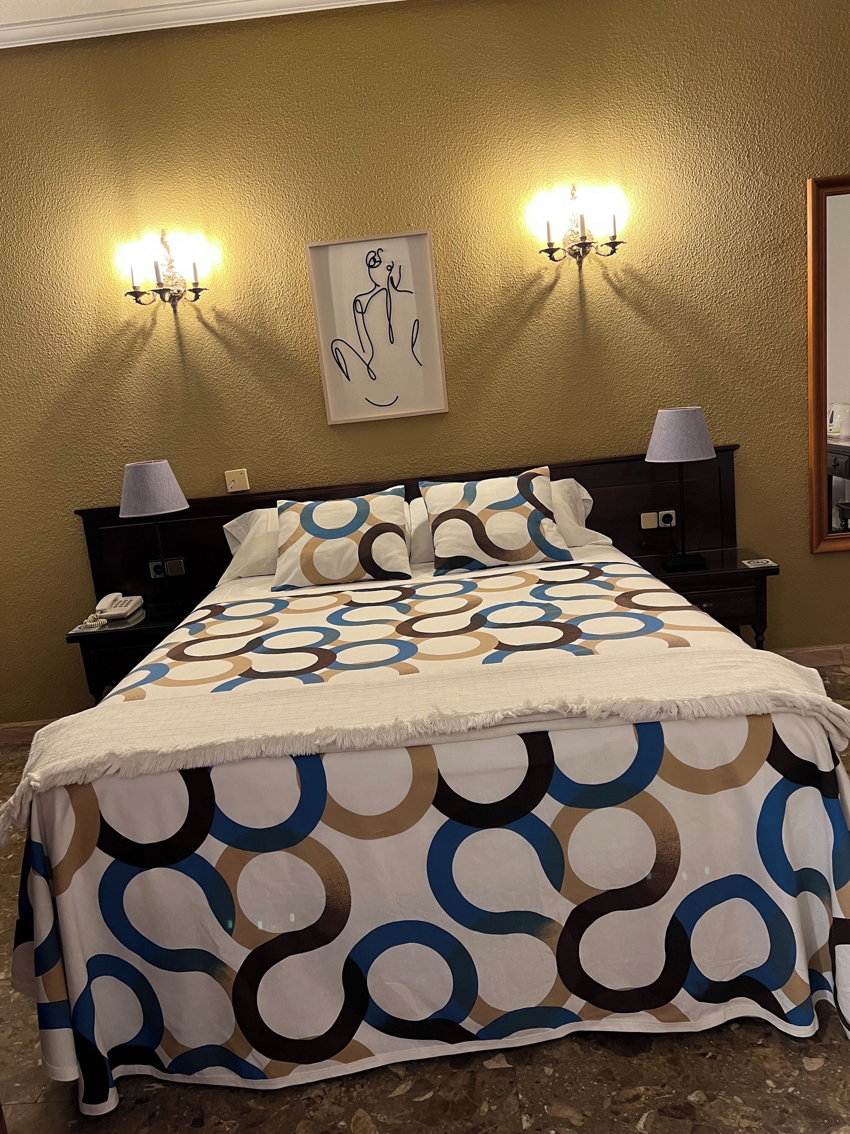 A hotel room with a bed, two bedside lamps, a wall-mounted artwork, and a telephone on the nightstand.