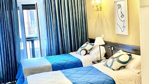 Habitación de hotel con dos camas, un candelabro, una obra de arte enmarcada en la pared y vistas al exterior.