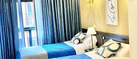 A hotel room with two beds, a chandelier, a framed artwork on the wall, and a view of the outside.