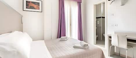 Habitación de hotel con cama, escritorio, silla, televisión y baño visible a través de una puerta abierta.