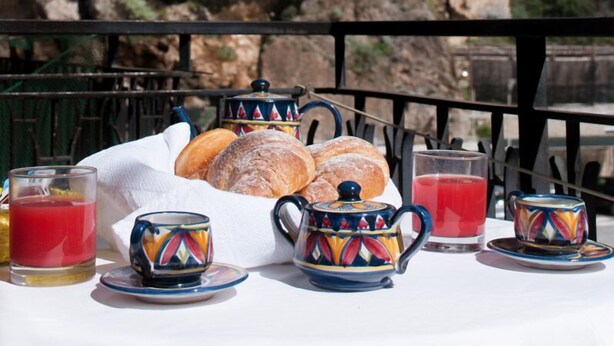 A breakfast setup with pastries, tea, and juice on a table, overlooking a cliff and a building with domed architecture. - Hotel De Rosa (Maiori)
