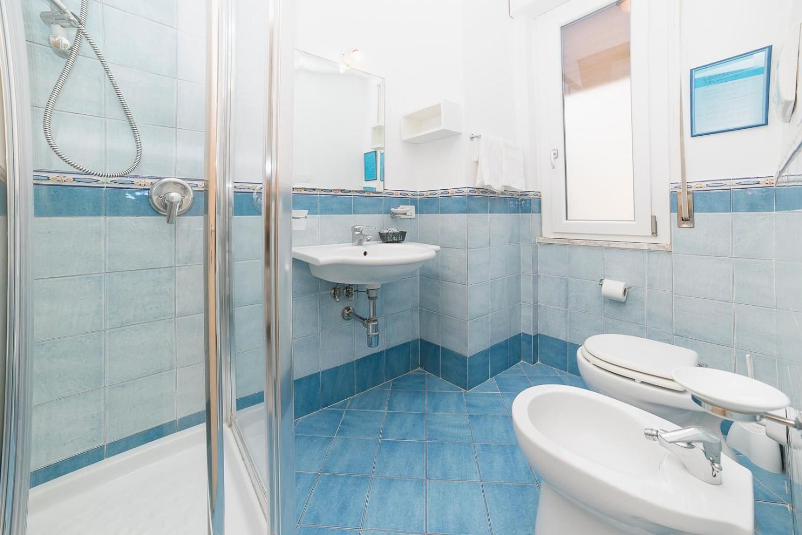 Un baño con cabina de ducha de vidrio, un lavabo, un inodoro y un bidé.