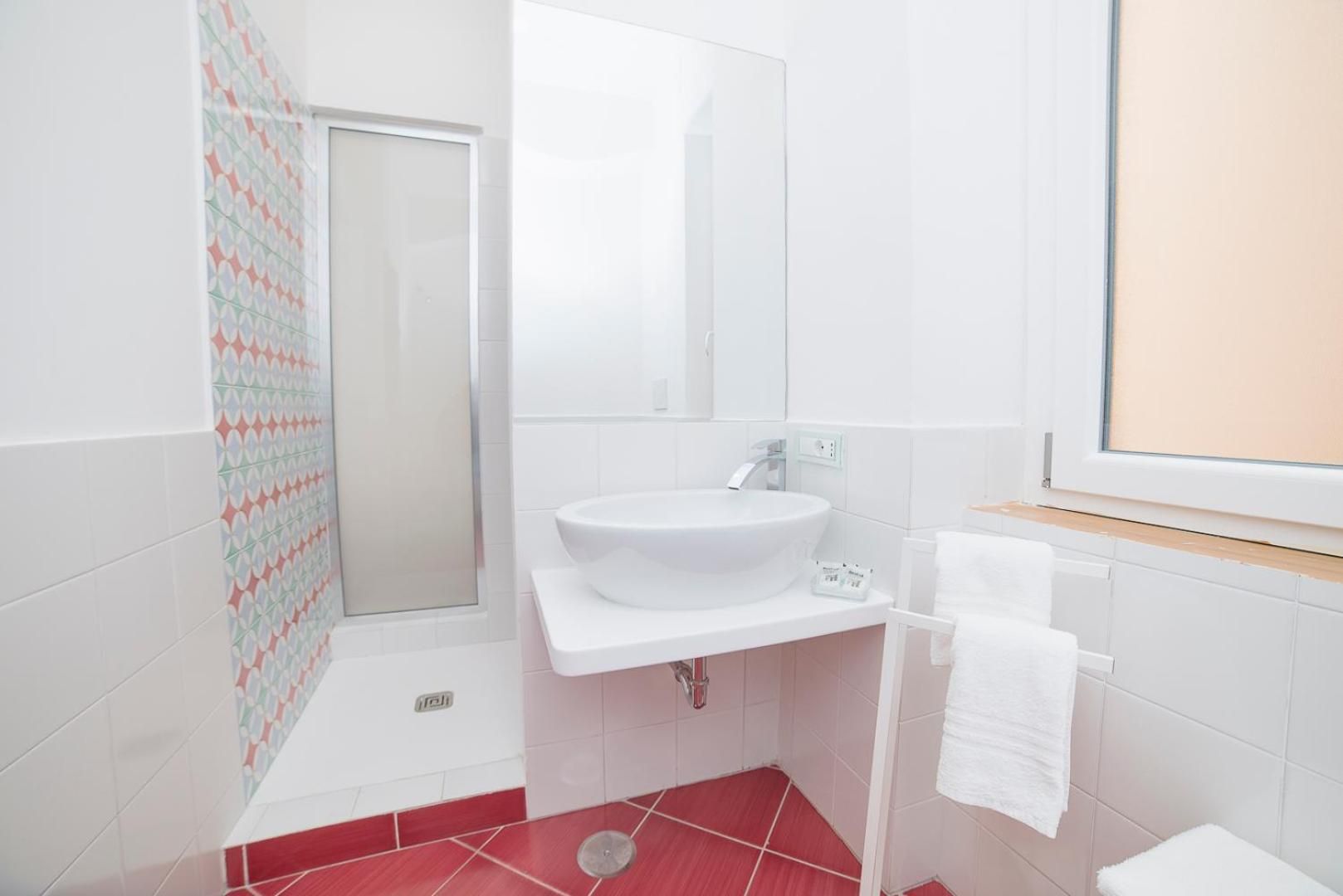 Un baño con un lavamanos blanco, un espejo, una ducha y una ventana.
