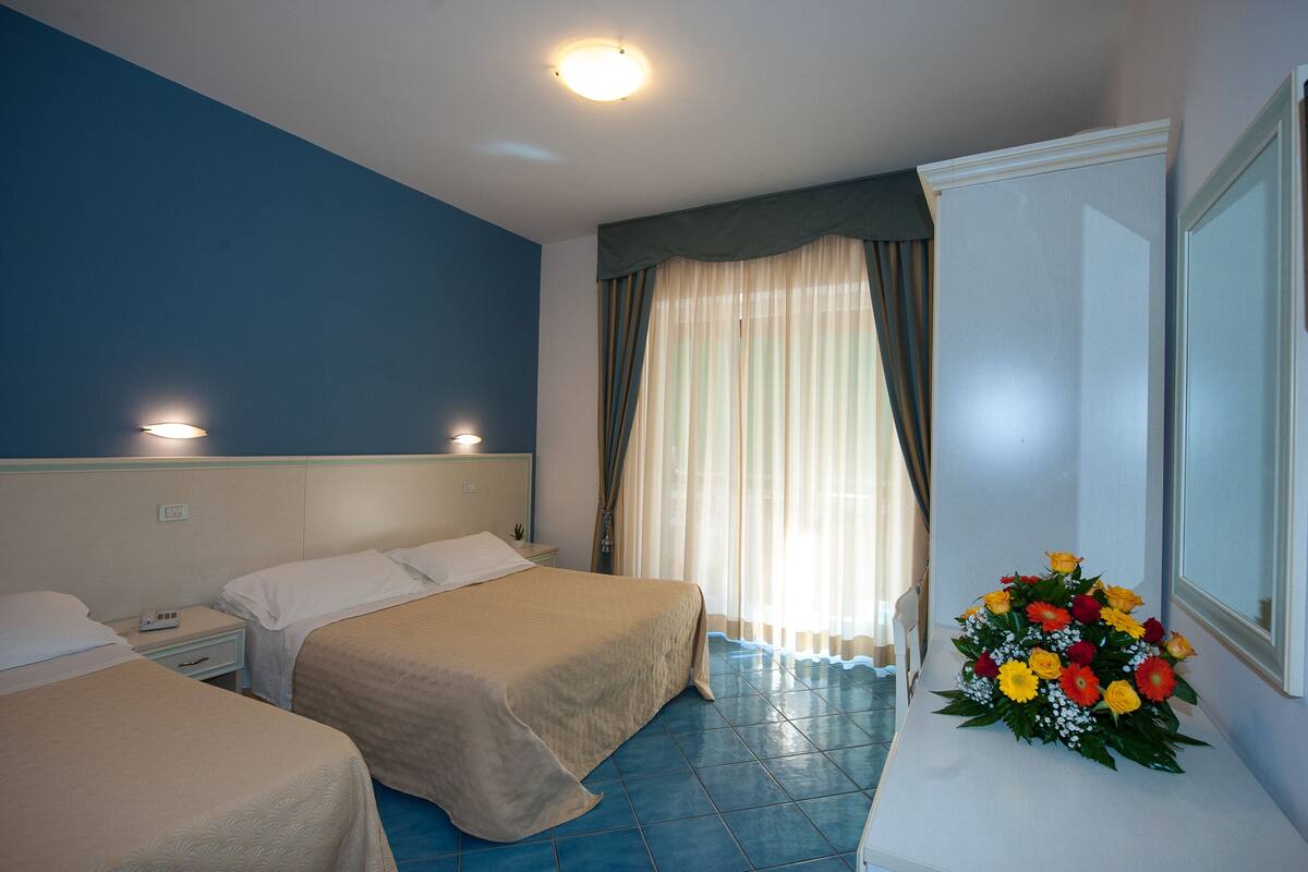 Habitación de hotel con dos camas, una mesita de noche y un arreglo floral.