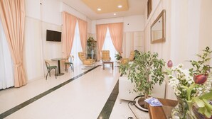 A hotel lobby with a seating area, a reception desk, and a television mounted on the wall. - Hotel De Rosa (Maiori)