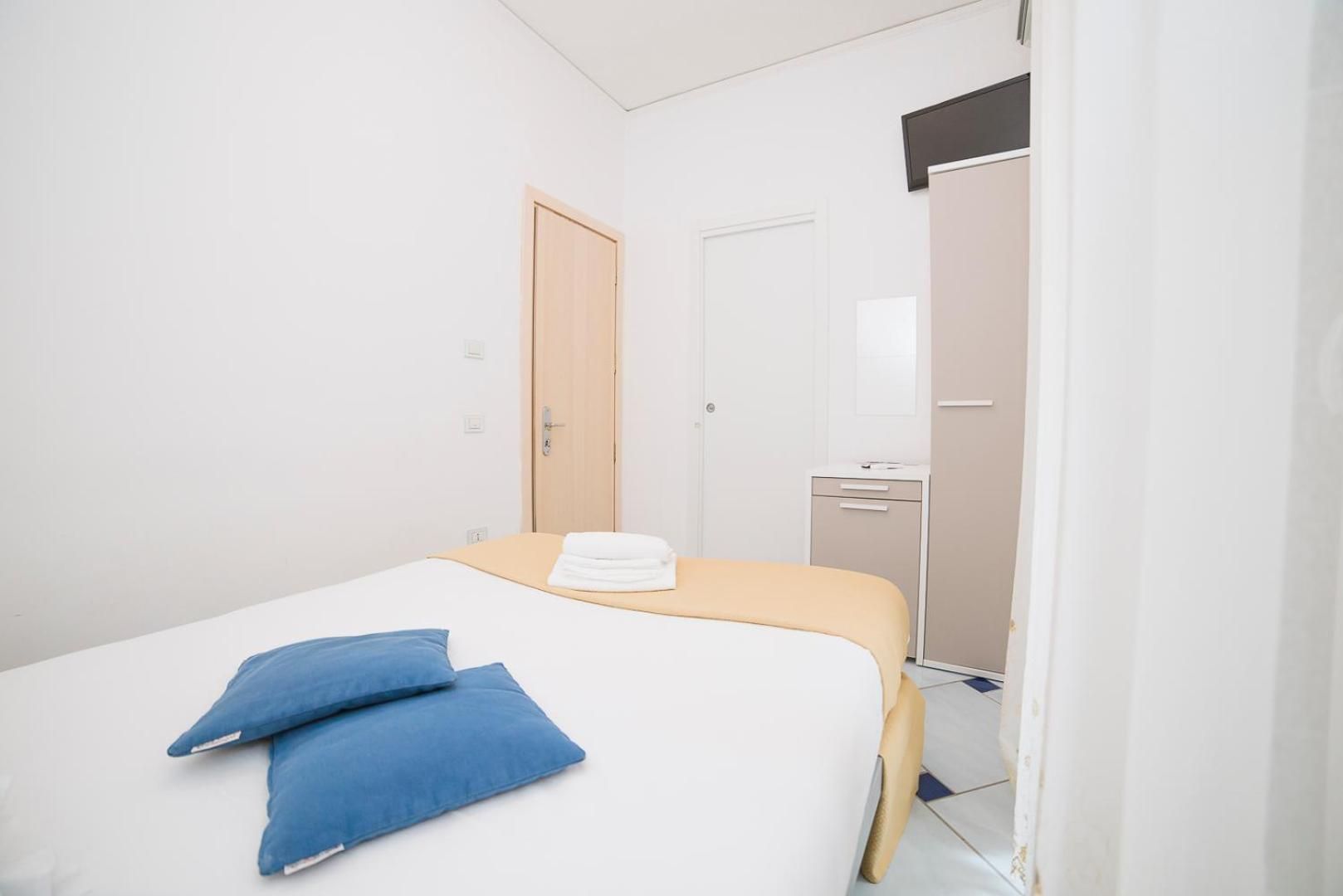Hotelkamer met een bed, twee kussens, een nachtkastje, een kledingkast en een spiegel.