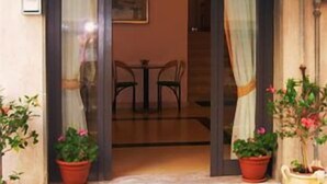 A hotel entrance with a sign reading "Alberto De Rosa". There are potted plants outside and a small table with chairs inside. - Hotel De Rosa (Maiori)