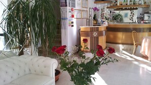 Un salon bien éclairé, avec un canapé blanc, une table basse et une grande plante en pot. On y trouve un comptoir de bar en bois, avec un téléviseur placé au-dessus et diverses bouteilles sur les étagères.