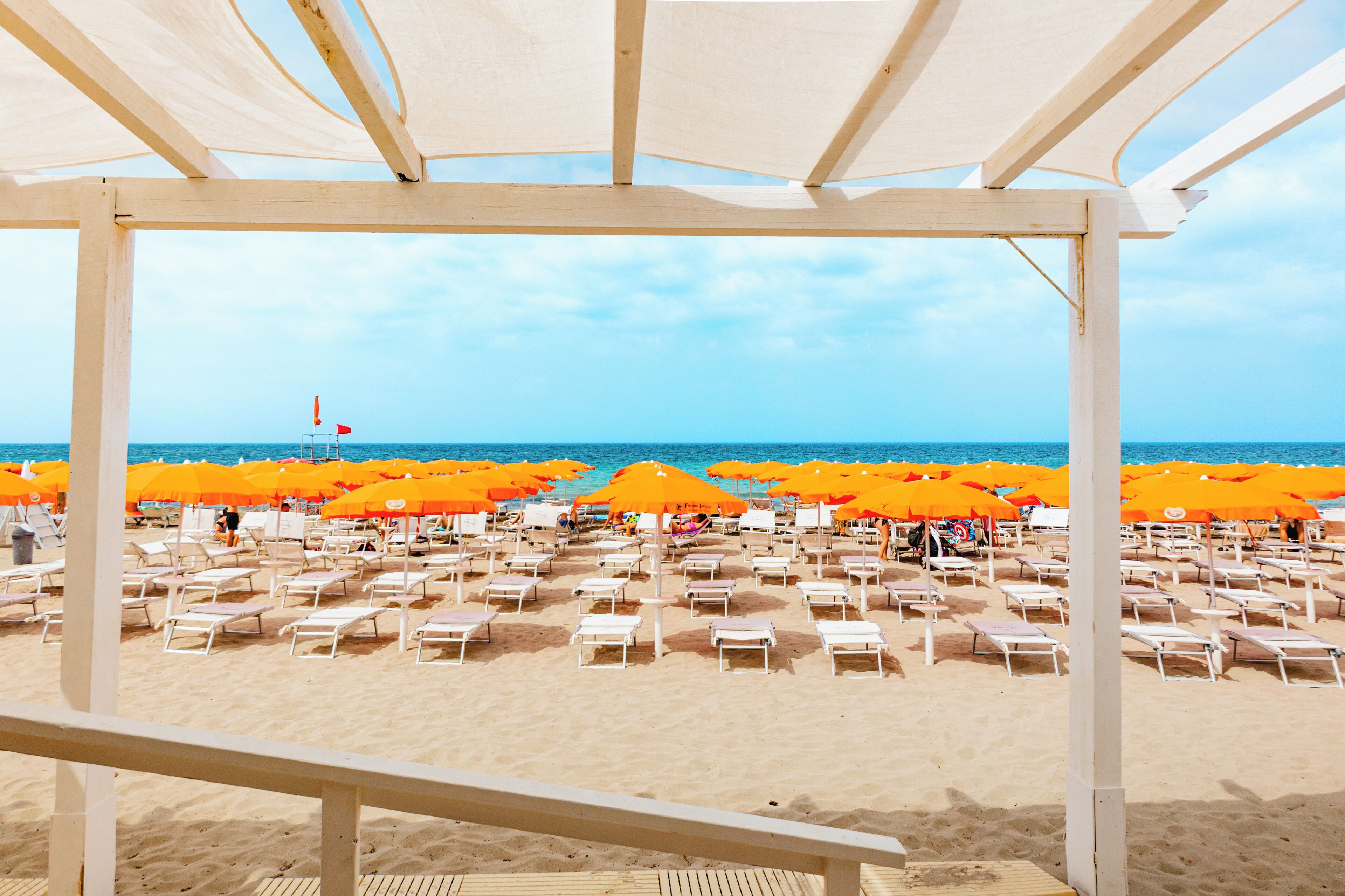 Una spiaggia con file di lettini e ombrelloni arancioni, un cielo sereno e il mare sullo sfondo.