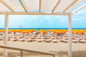 A beach with rows of sun loungers and orange umbrellas, a clear sky, and the sea in the background. - Delfino Beach Hotel (Marsala)